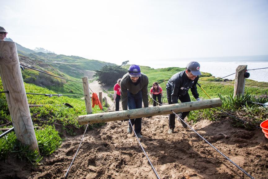 4 people help install fencing on a coastal trail