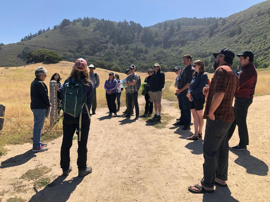 A group of people stand in a circle at a diverging trail on an open hillside