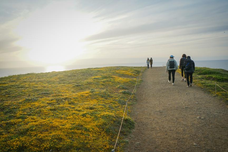 people walking an open hilltop trail into the sunset