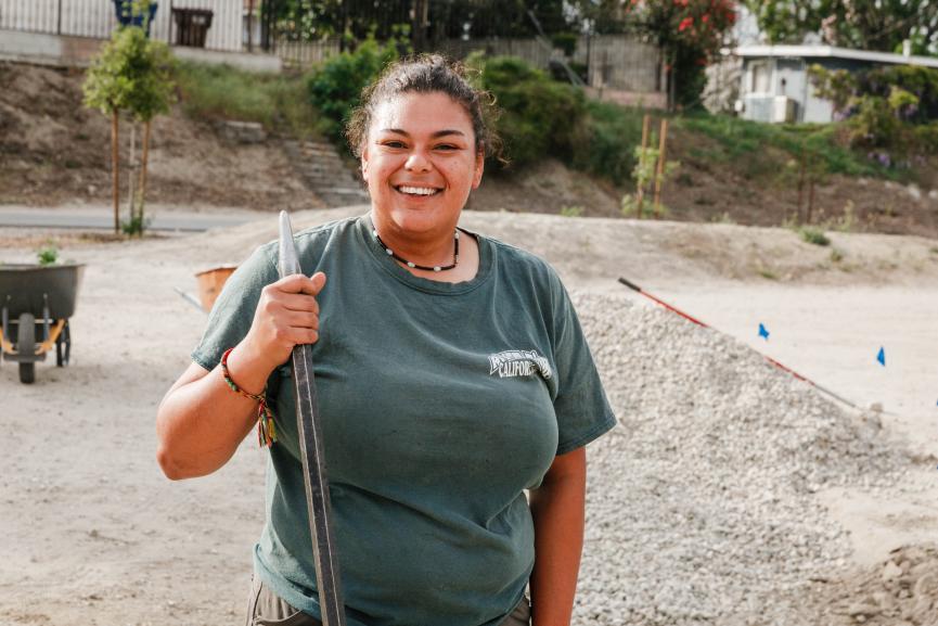 woman standing holding a shovel and smiling in an urban green restoration site